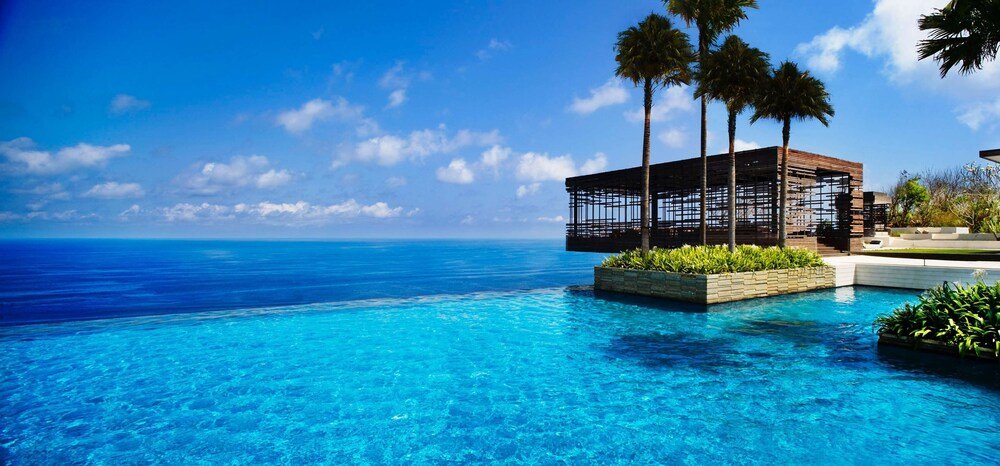 Clear blue pool with a wooden structure and palm trees at Alila Villas Uluwatu